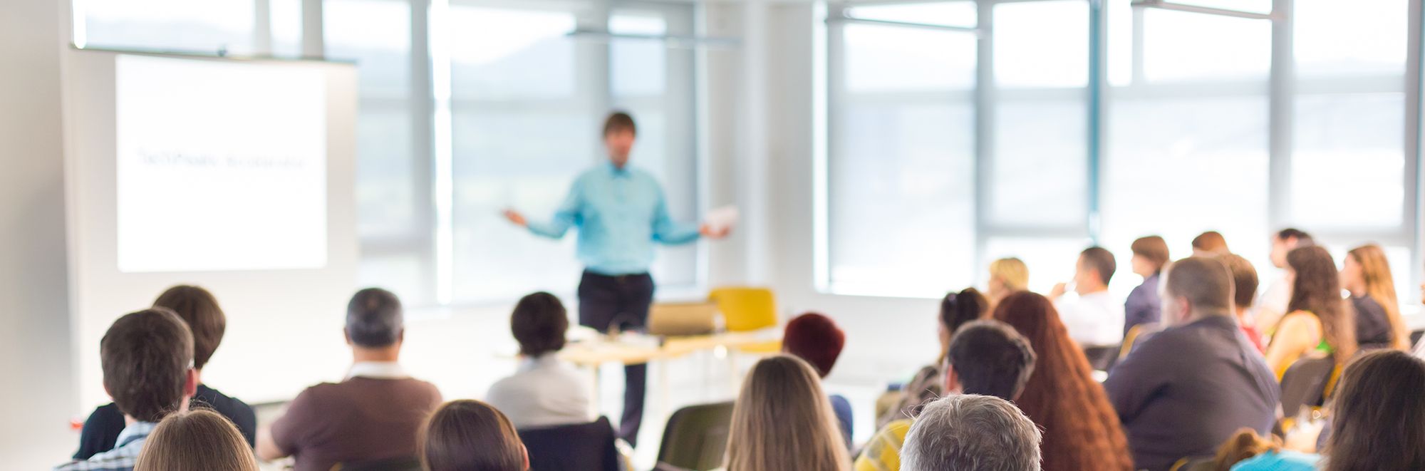 Mehrere Personen in einem Seminarraum. Ein Sprecher spricht über ein Thema.