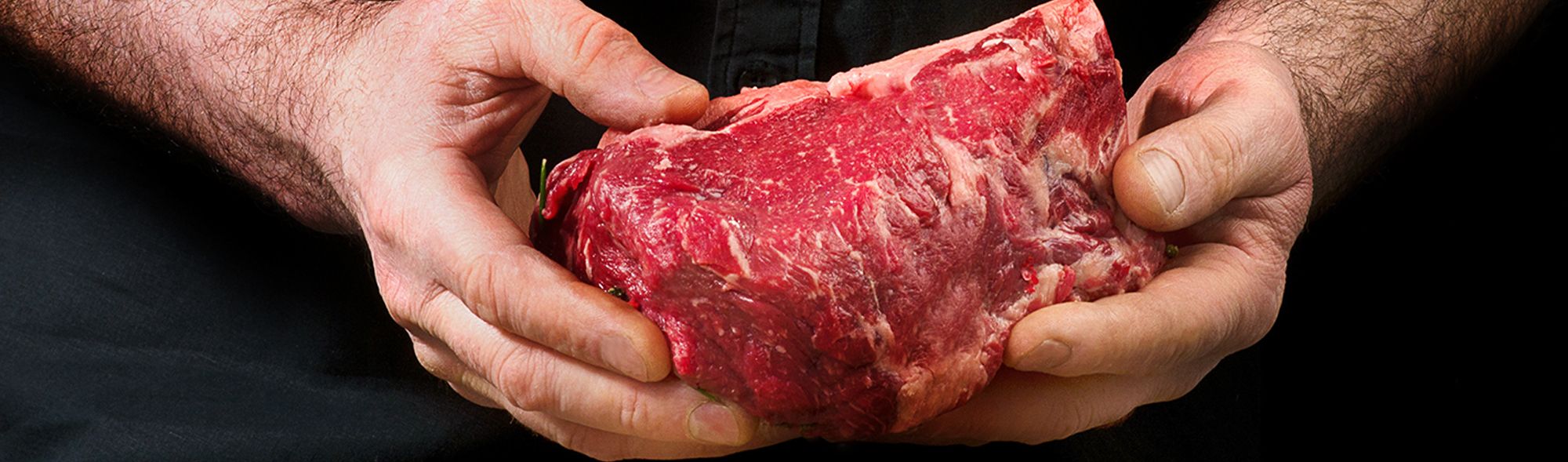 Frisches Stück rohes Fleisch wird von Hand präsentiert – Symbol für Qualität und Handwerk.